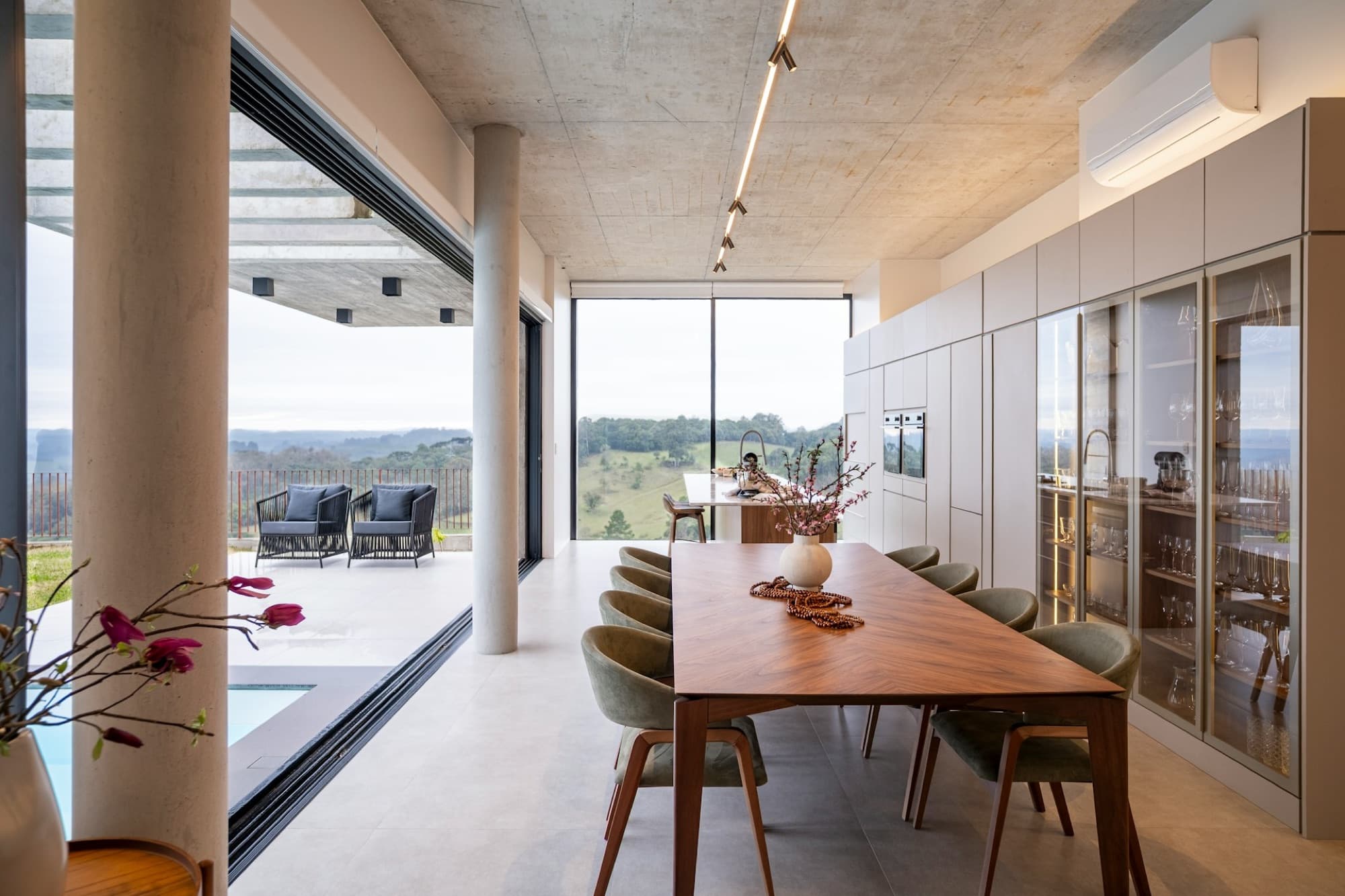 Long walnut dining table beside floor-to-ceiling glazing overlooking the hills